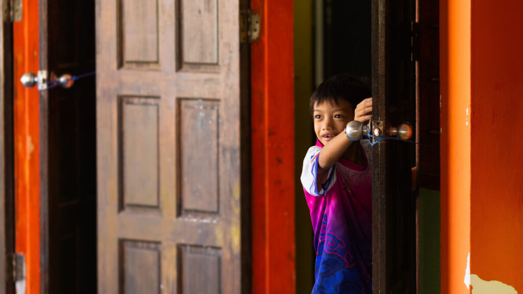 young boy peeking through a door in Borneo
