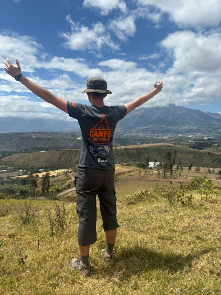 A traveller boy standing on a hill with his arms up in the air in Ecuador