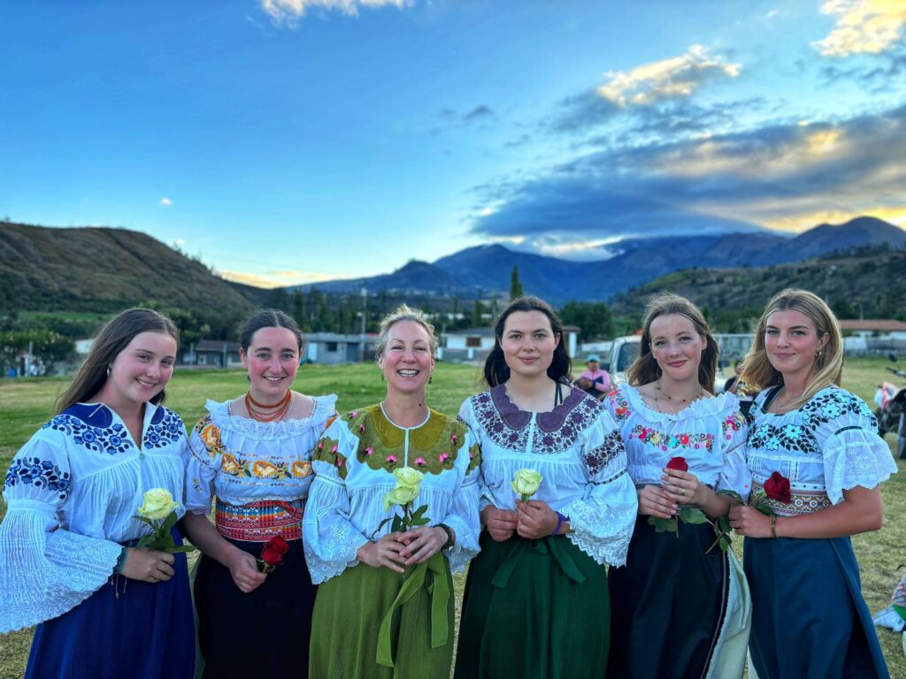 Group of student travellers dressed in traditional clothing from Ecuador holding white roses standing in front of a mountain range