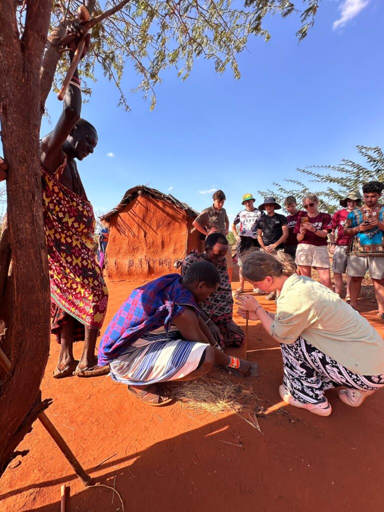 student travellers visiting the maasai tribe building fire together in Kenya