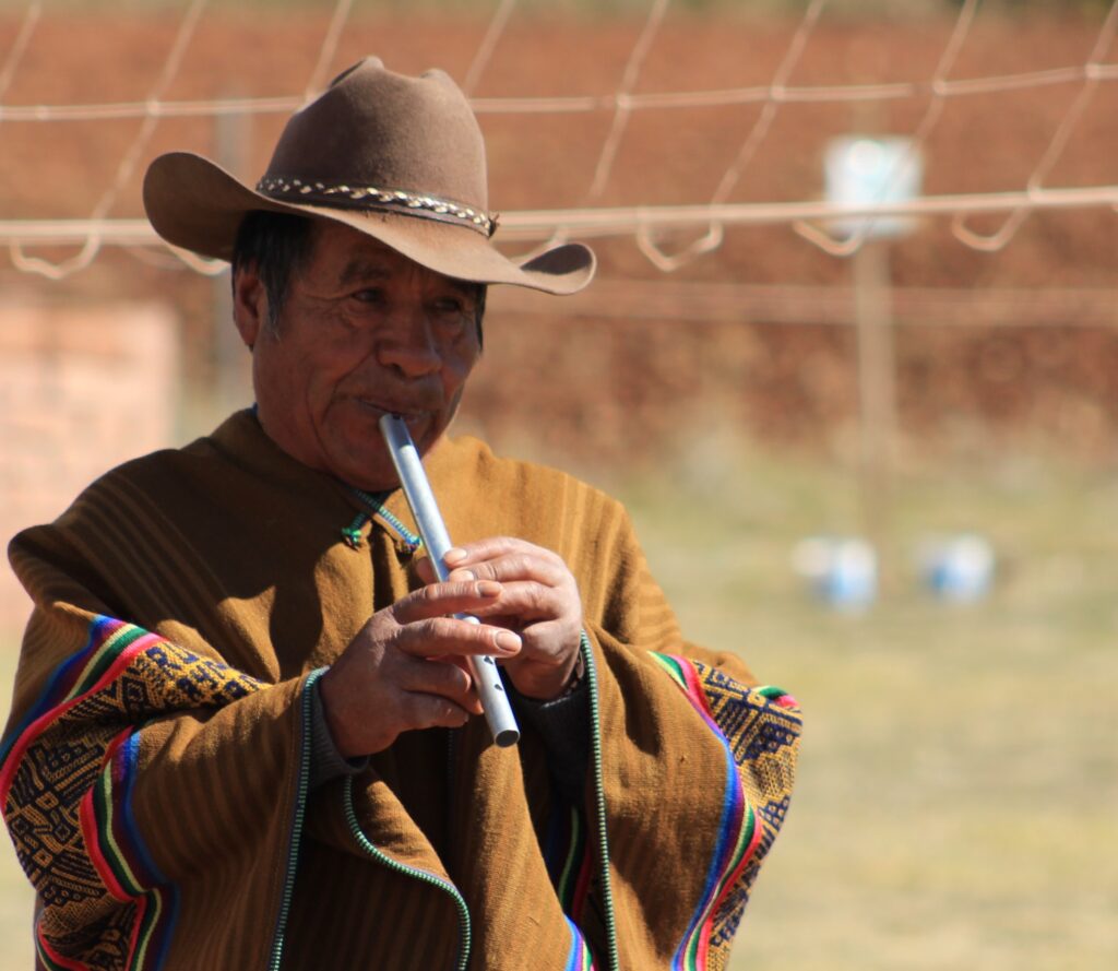 a local peruvian man wearing a hat and a poncho playing a flute