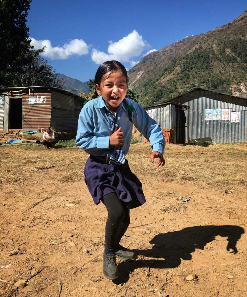 little girl in Nepal laughing outside with mountains in the background