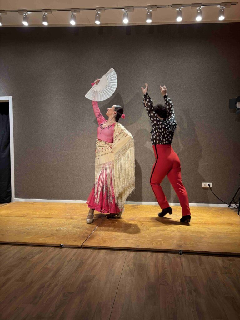 Pair of man and woman dancing flamingo. Man is wearing red pants with back top while woman is wearing pink dress and holding a fan.