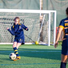 A young female student wearing a soccer uniform kicking the soccer ball in a soccer practice.