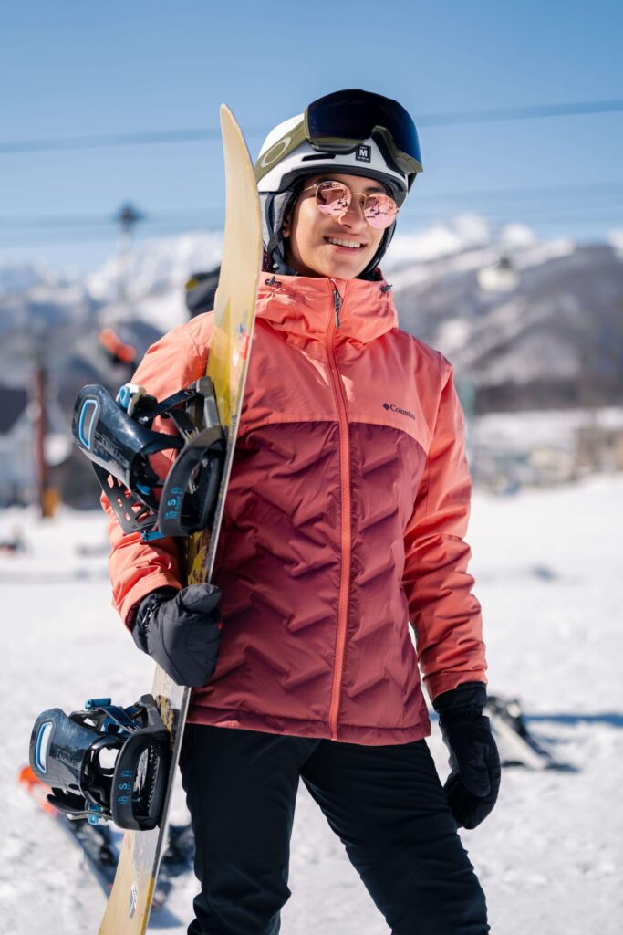A solo picture of a skier wearing ski gear but holding the snowboard on his right hand.