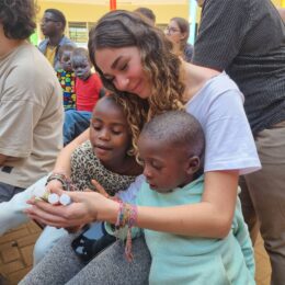 Woman with two children in her arms while she is showing them bottles of glitter as craft materials.