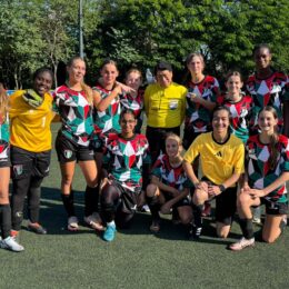 A group of young soccer athletes together with their coaches posing in the field.
