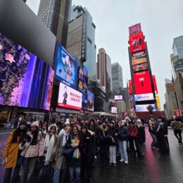 Group of students in the middle of New York Times Square, with flashing billboards around them.