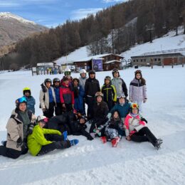 Group of about kids and teens gathered on a snowy ski slope, posing together for a group picture dressed in winter gear.